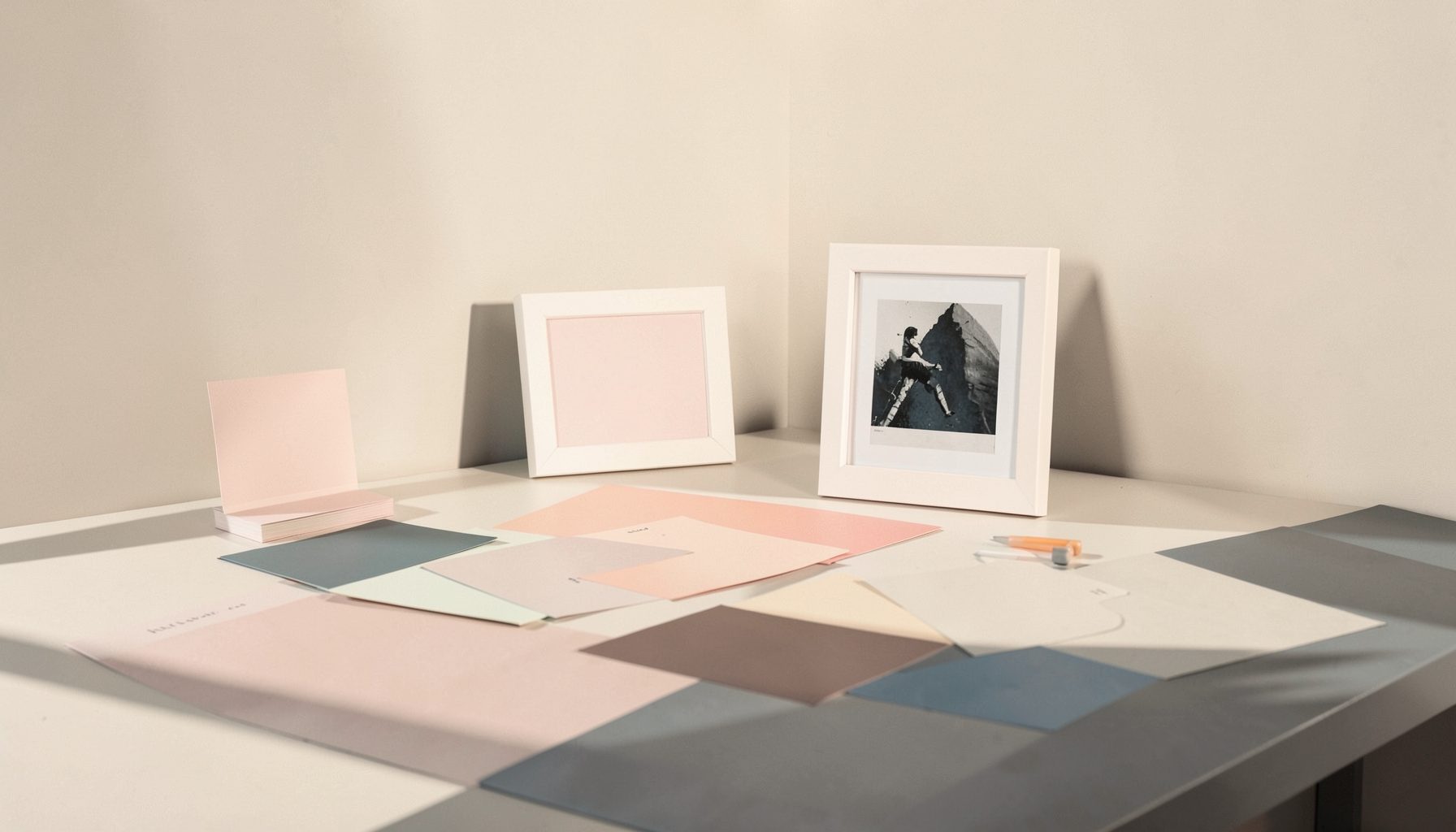 A softly lit studio table with color swatches and small framed studies in blush pink and slate blue