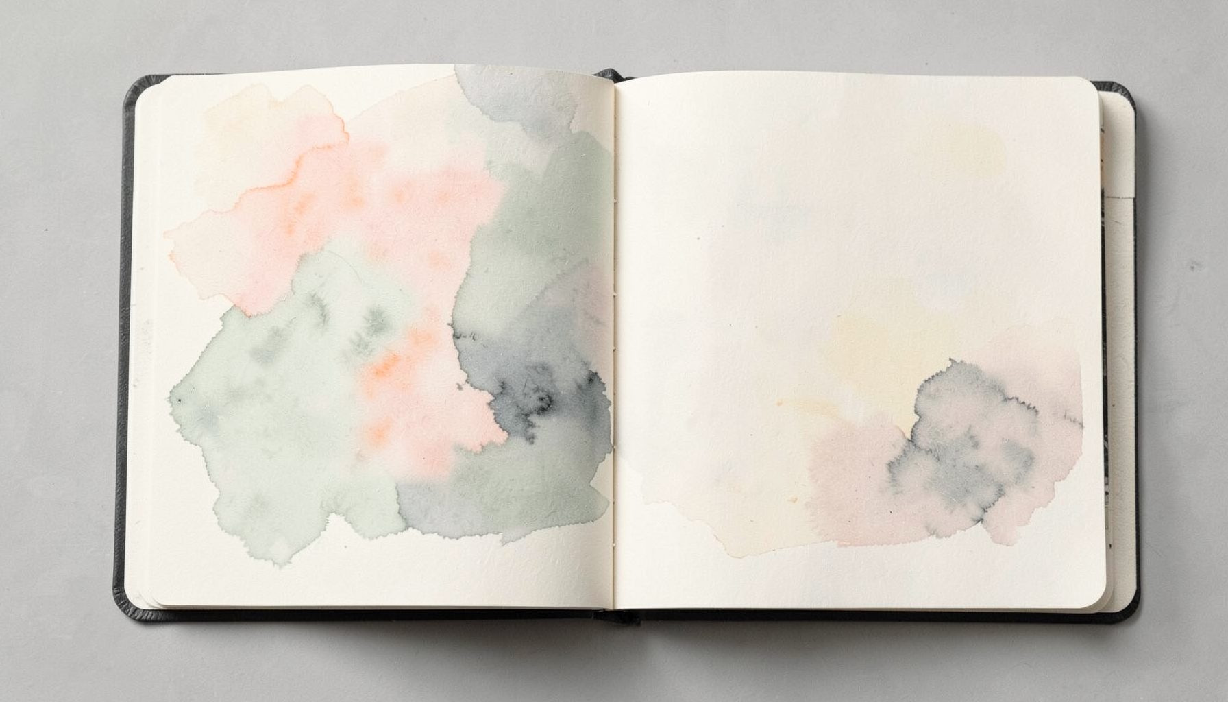 An open sketchbook with delicate watercolor washes in pale rose and sage