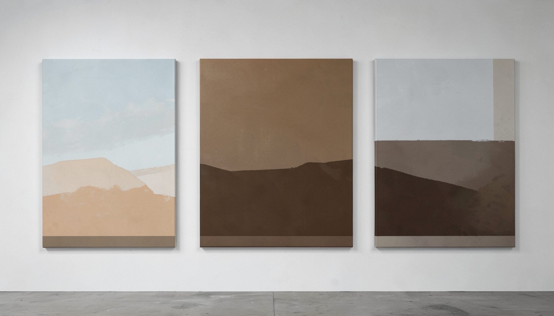 A gallery wall with three large-scale canvases in soft earth tones and pale blue